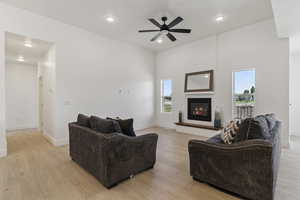 Living room featuring ceiling fan, light wood finished floors, a glass covered fireplace, recessed lighting, and a high ceiling