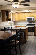 Kitchen featuring stainless steel appliances, wood-style flooring, tasteful backsplash, light stone counters, and a kitchen bar