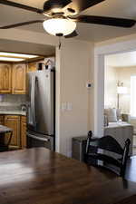 Kitchen with wood finish cabinetry, stainless steel refrigerator with ice dispenser, a ceiling fan, and tasteful backsplash