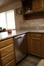 Kitchen with stainless steel dishwasher, light stone countertops, decorative backsplash, and wood finish cabinetry