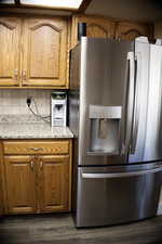 Kitchen featuring stainless steel refrigerator with ice dispenser, light stone counters, wood finish cabinetry, and wood-style floors