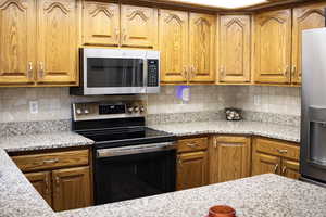 Kitchen with stainless steel appliances, wood finish cabinetry, and decorative backsplash