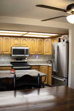 Kitchen with stainless steel appliances, ceiling fan, tasteful backsplash, wood finish cabinets, and light stone counters