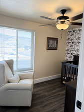Bedroom with a nursery area, wood-style floors, ceiling fan, and a textured ceiling
