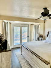 Bedroom with a textured ceiling, access to outside, dark wood-type flooring, and ceiling fan