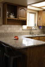 Kitchen featuring stone counters, a kitchen bar, a peninsula, backsplash, and wood finish cabinets