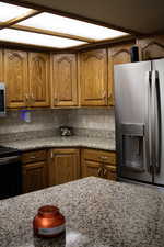 Kitchen featuring stainless steel appliances, wood finish cabinets, light stone counters, and backsplash