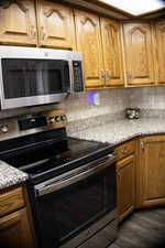 Kitchen with stainless steel appliances, wood finish cabinetry, light stone countertops, and backsplash