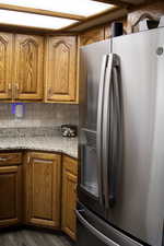 Kitchen with stainless steel fridge, wood finish cabinets, light stone countertops, tasteful backsplash, and wood-type flooring