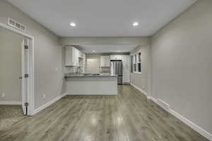 Kitchen featuring white cabinetry, a peninsula, freestanding refrigerator, light stone countertops, and light wood-style flooring