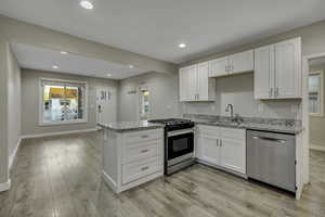 Kitchen featuring stainless steel appliances, white cabinetry, light stone countertops, a peninsula, and light wood finished floors