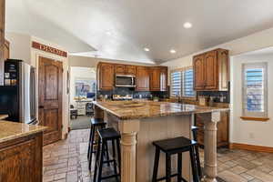 Kitchen featuring stainless steel appliances, wood finish cabinets, stone tile floors, a center island, and tasteful backsplash