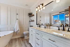 Bathroom with a soaking tub, double vanity, light wood-type flooring, crown molding, and a decorative wall