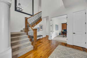 Stairway featuring hardwood / wood-style floors, a high ceiling, ornate columns, and a chandelier