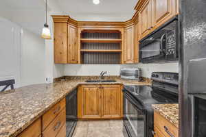 Kitchen with black appliances, dark stone counters, open shelves, wood finish cabinetry, and hanging light fixtures