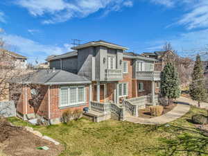 Back of house with brick siding, a balcony, a lawn, and roof with shingles