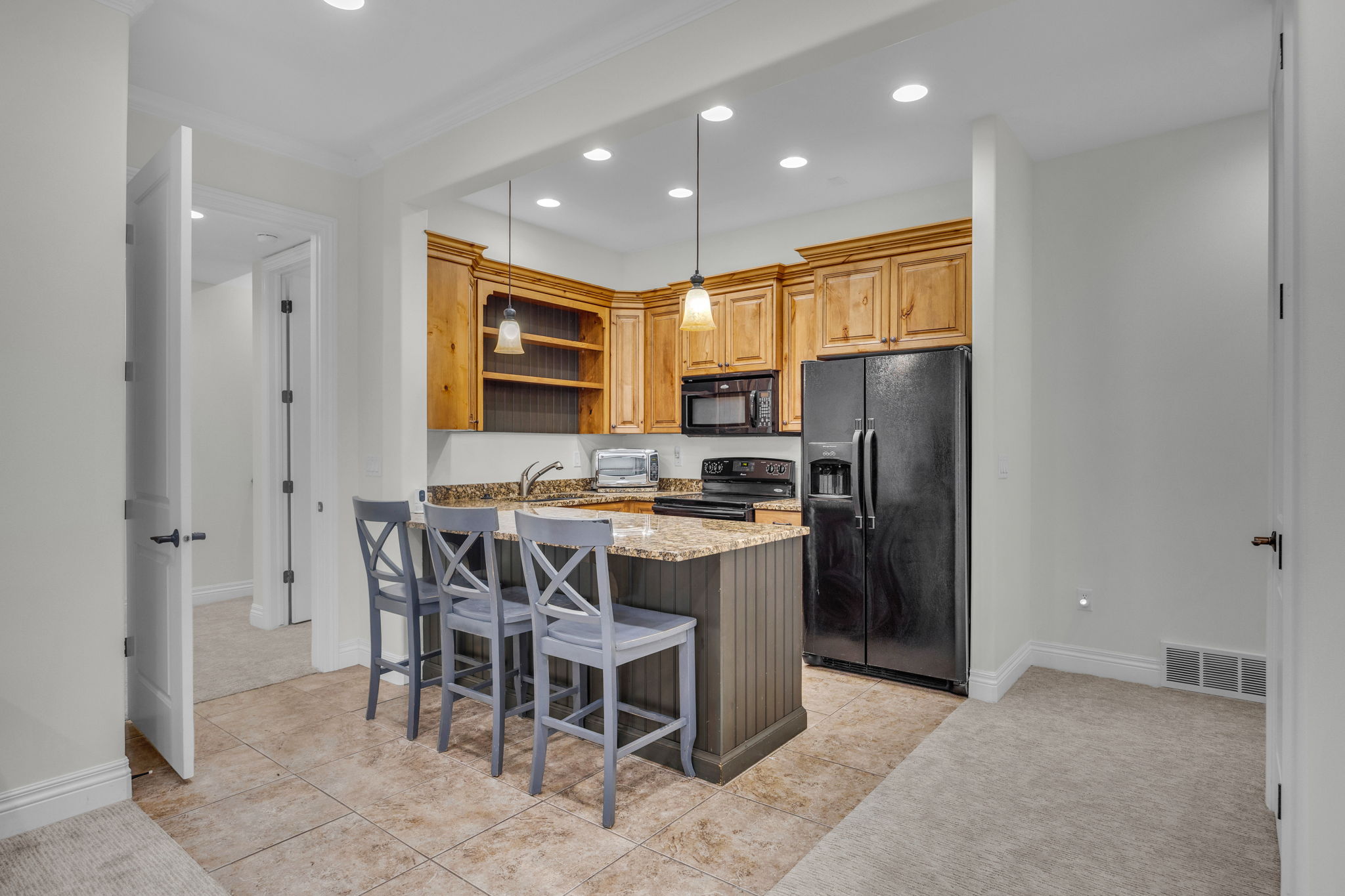 Kitchen with light stone countertops, black appliances, a kitchen breakfast bar, open shelves, and a peninsula
