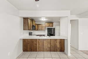Kitchen with light countertops, black appliances, wood finish cabinetry, light tile patterned floors, and a peninsula