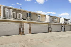 Back of property with a balcony, brick siding, driveway, and a garage