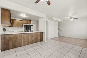 Kitchen with a ceiling fan, wood finish cabinetry, light countertops, and light tile patterned floors