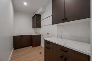 Laundry room with hookup for a washing machine, cabinet space, and light wood-style floors
