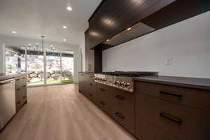 Kitchen with stainless steel appliances, hanging lights, modern cabinets, light wood-type flooring, and dark stone counters