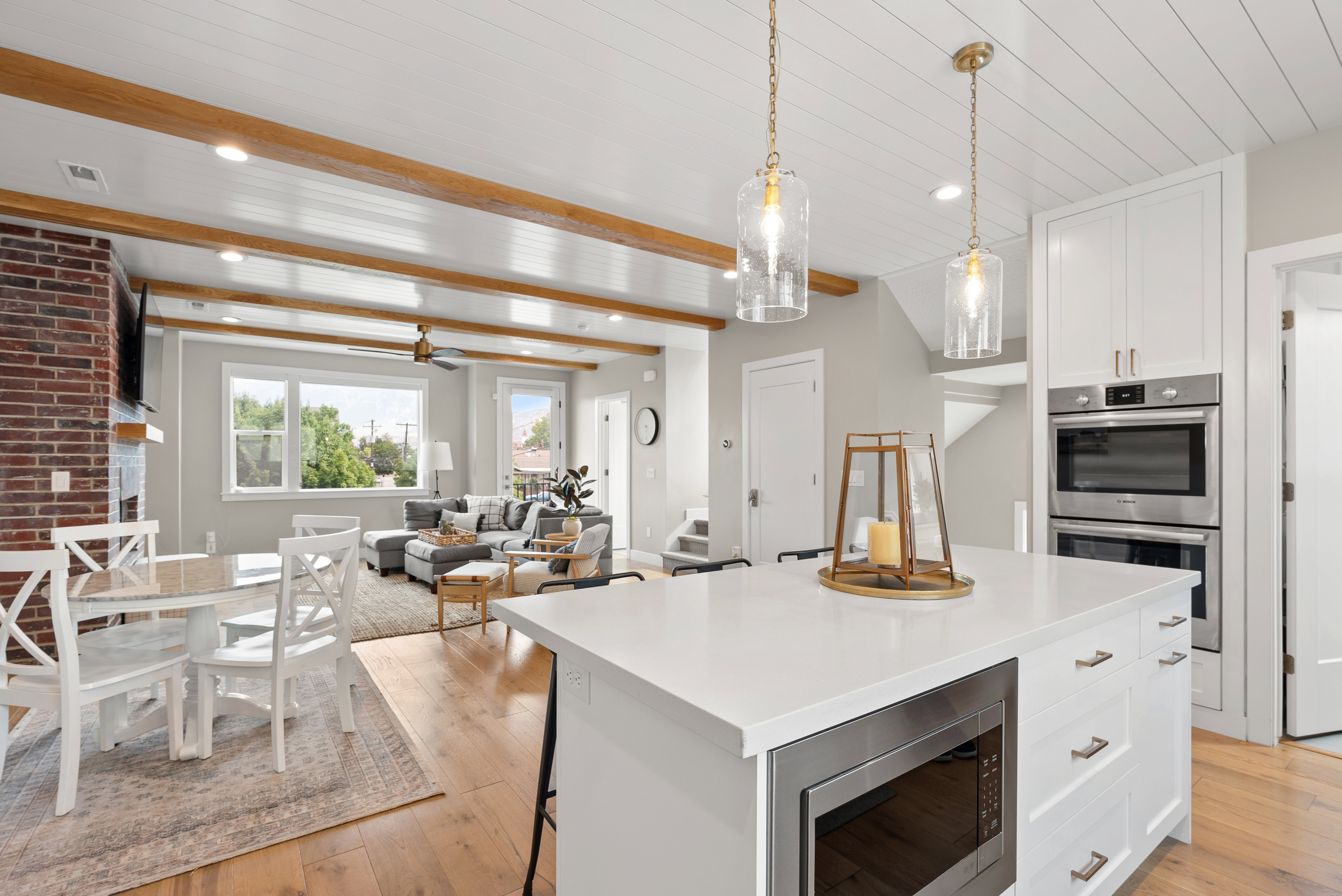 Kitchen featuring white cabinets, open floor plan, stainless steel appliances, decorative light fixtures, and beam ceiling