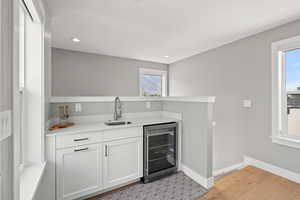 Bar area featuring white cabinetry, wine cooler, light wood-type flooring, recessed lighting, and light stone counters