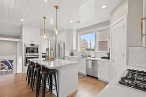 Kitchen featuring a kitchen breakfast bar, stainless steel appliances, white cabinetry, light wood-type flooring, and a kitchen island