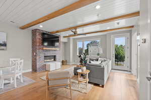 Living area featuring a ceiling fan, light wood-style floors, a fireplace, recessed lighting, and a wooden ceiling with exposed beams