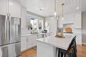 Kitchen featuring stainless steel appliances, white cabinets, a center island, light wood-style flooring, and a kitchen bar