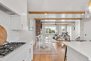 Kitchen featuring open floor plan, white cabinetry, stainless steel gas stovetop, extractor fan, and light wood-style flooring