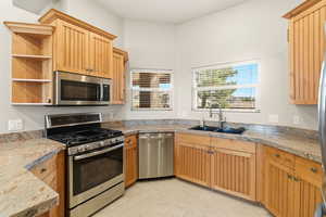 Kitchen featuring stainless steel appliances, open shelves, light stone counters, and light wood finish cabinetry