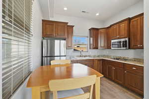 Kitchen featuring stainless steel appliances, light stone counters, wood finish floors, and wood finish cabinets