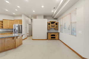 Kitchen with open shelves, stainless steel fridge with ice dispenser, recessed lighting, dark stone counters, and a breakfast bar area