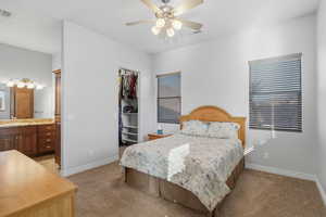 Bedroom with a spacious closet, light carpet, a ceiling fan, and connected bathroom