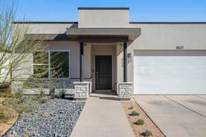 Entrance to property with stucco siding, concrete driveway, and stone siding
