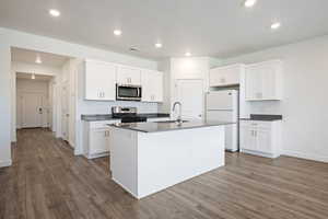 Kitchen with dark countertops, stainless steel appliances, white cabinetry, a kitchen island with sink, and recessed lighting