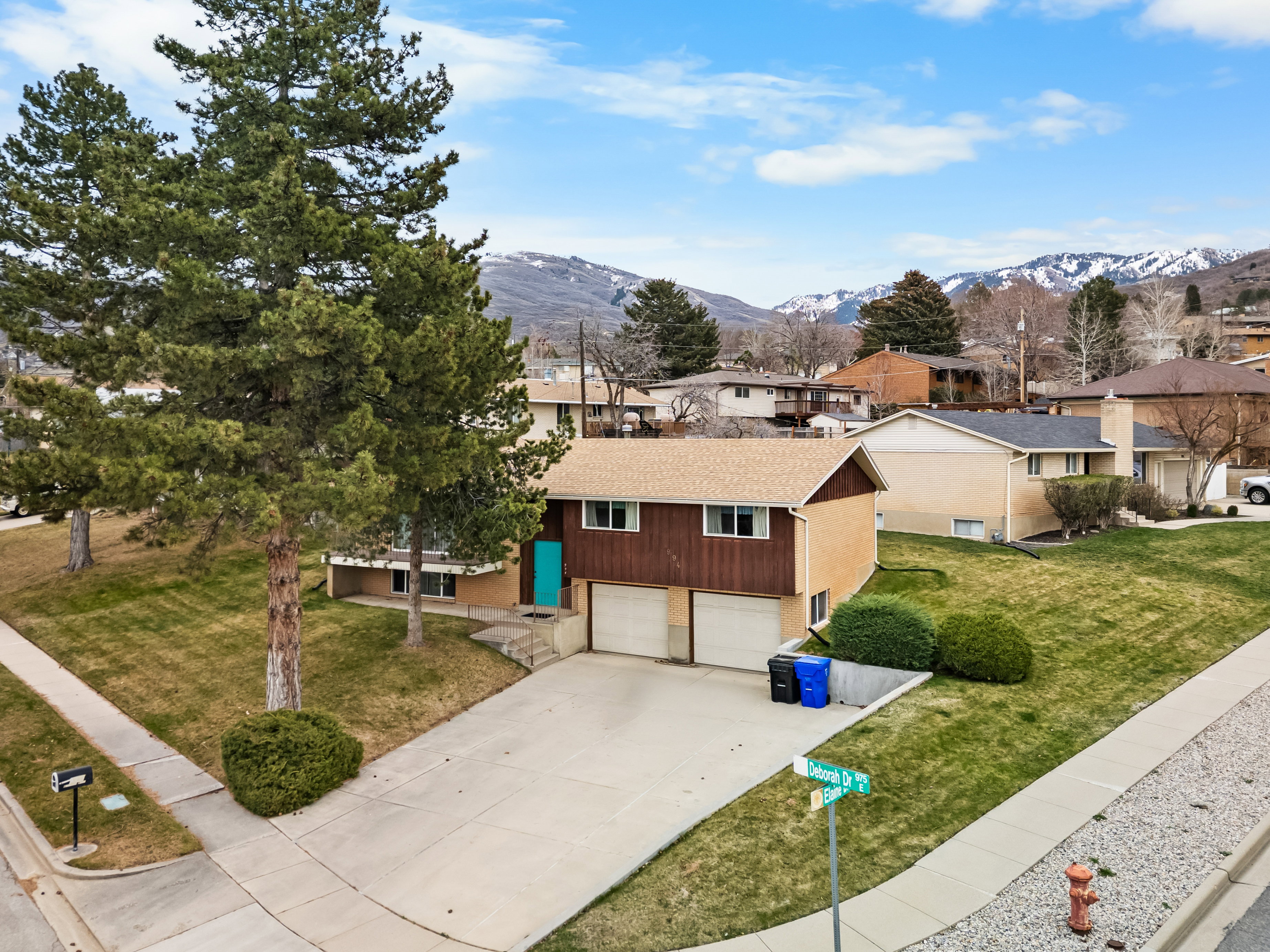 View of front of house with concrete driveway, a residential view, a mountain view, and a front lawn