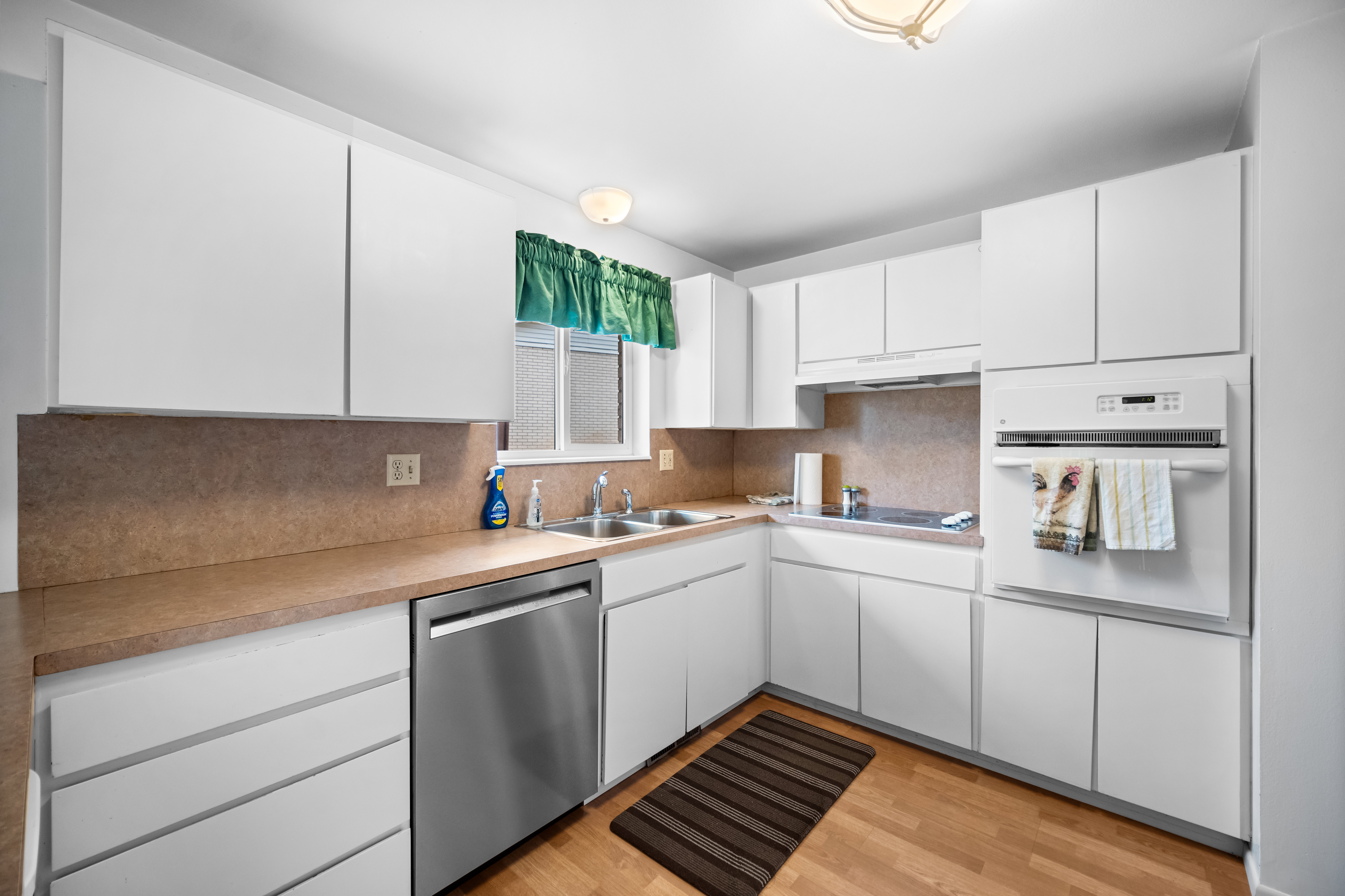 Kitchen with white cabinets, white oven, dishwasher, light wood-style floors, and light countertops