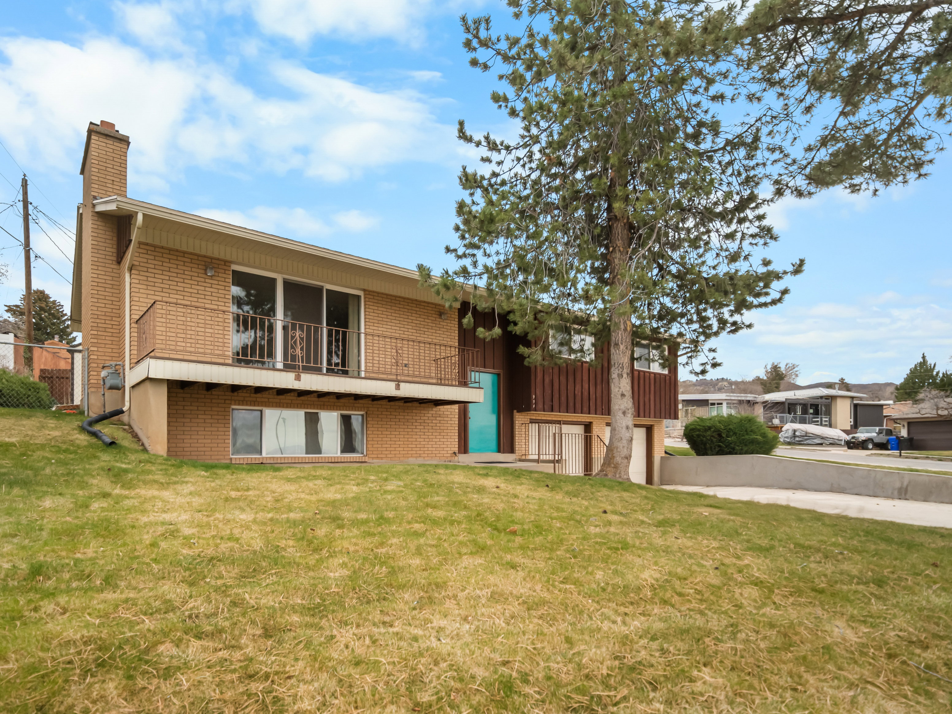 Back of property featuring a balcony, brick siding, a garage, a chimney, and concrete driveway