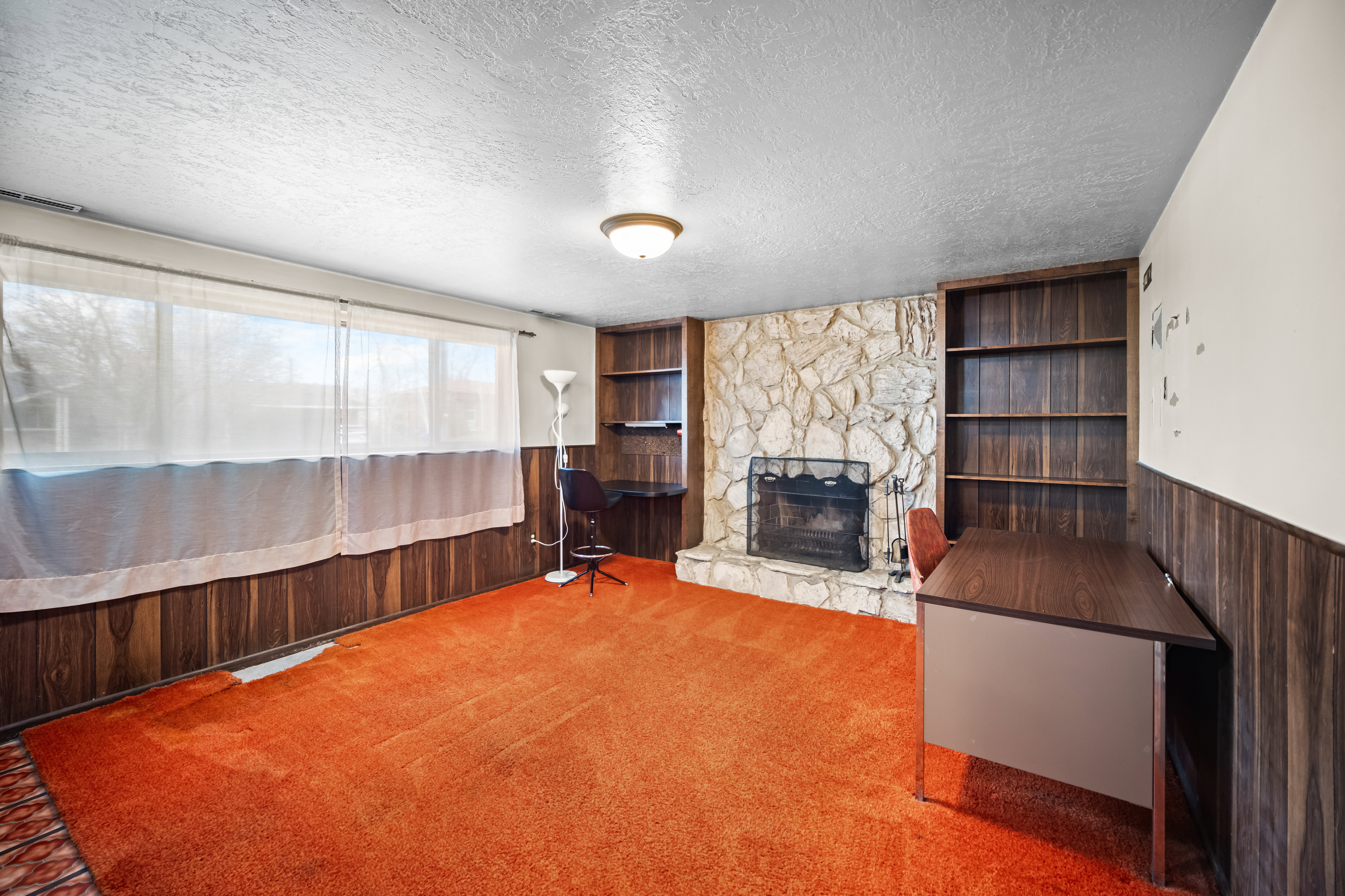 Living room with wainscoting, wooden walls, built in features, a fireplace, and a textured ceiling