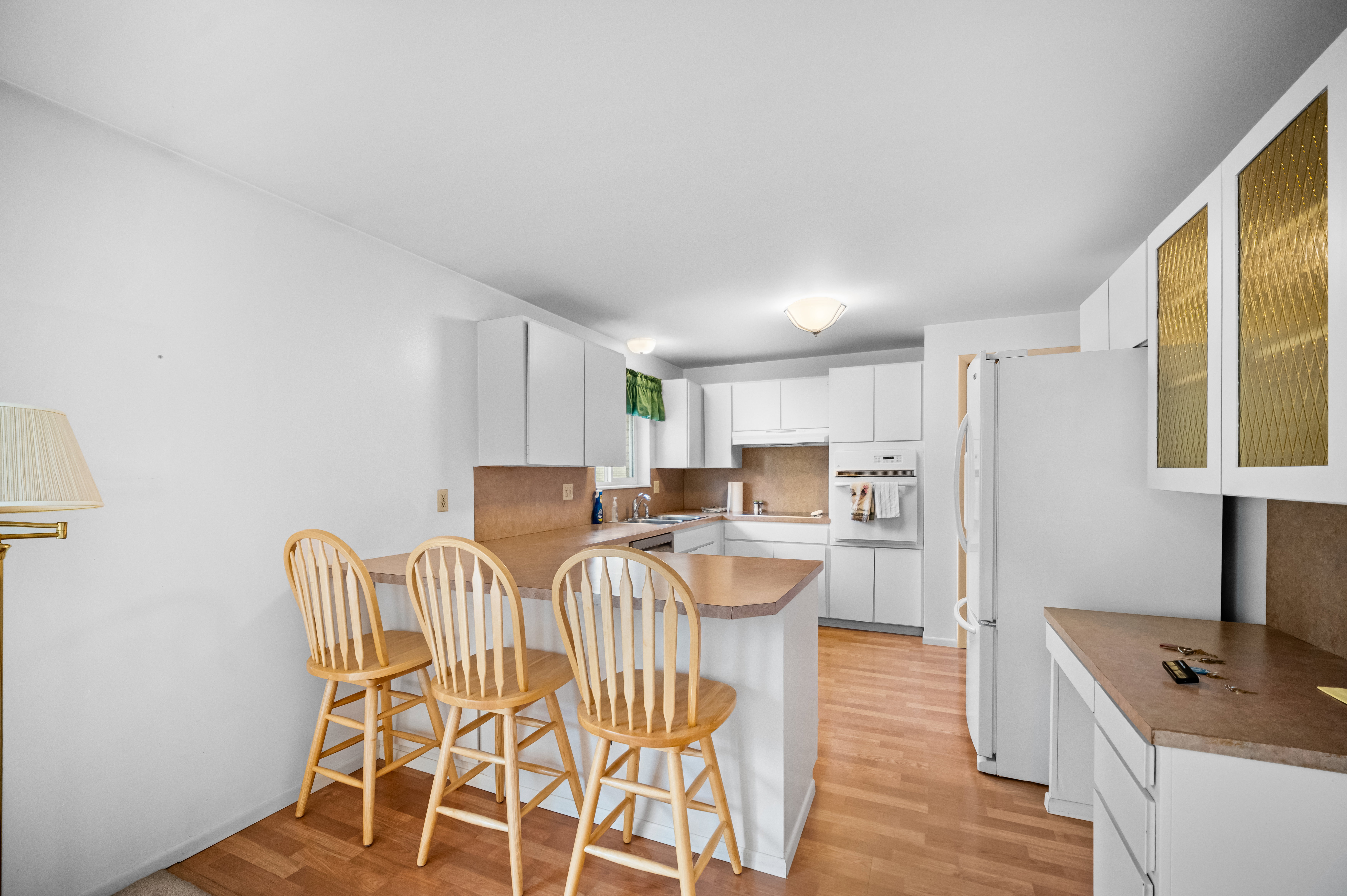 Kitchen featuring a breakfast bar area, white appliances, white cabinetry, light wood-style flooring, and glass insert cabinets