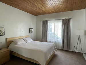 Carpeted bedroom featuring wood ceiling and a baseboard heating unit