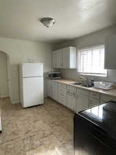 Kitchen featuring black electric range oven, freestanding refrigerator, light countertops, and stainless steel microwave