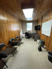 Office with wood walls, light colored carpet, and wooden ceiling