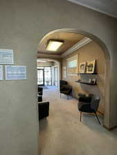 Corridor with arched walkways, wood ceiling, light colored carpet, crown molding, and a textured wall