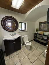 Bathroom featuring vanity, wood walls, a vaulted wood ceiling, and light tile patterned flooring