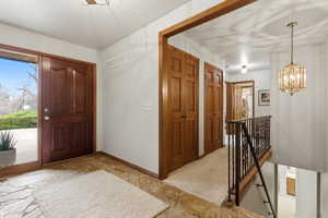 Foyer featuring suspended lighting, light stone finish flooring, and light carpet