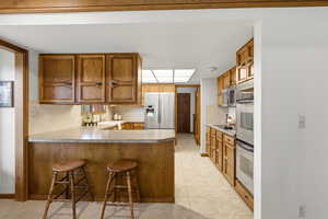 Kitchen featuring a peninsula, wood finish cabinets, a kitchen bar, and light countertops